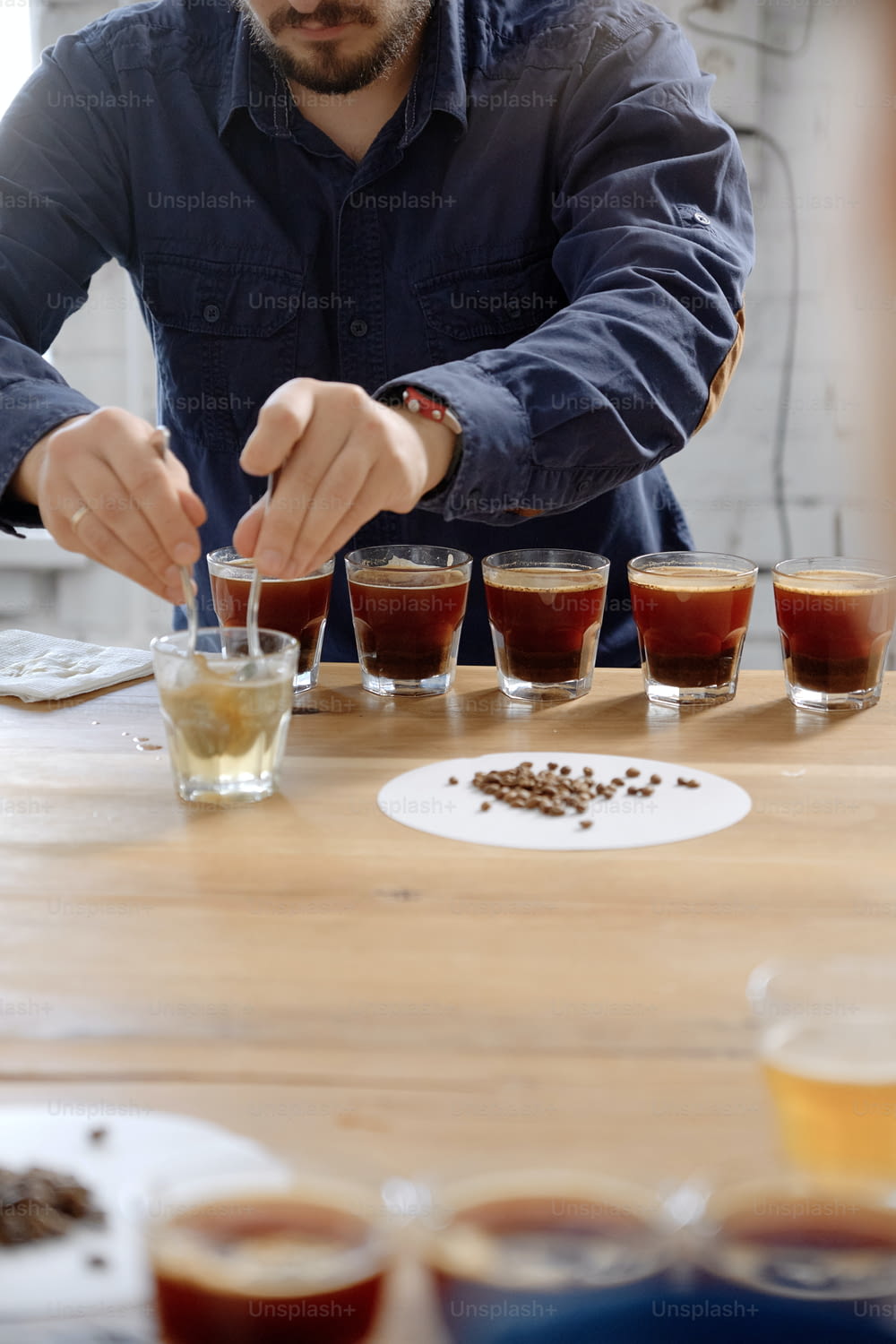 Close up of man's hands tasting freshly brewed coffee in glass cup, using spoon, examining coffee taste and flavour at coffee cupping test for barosta