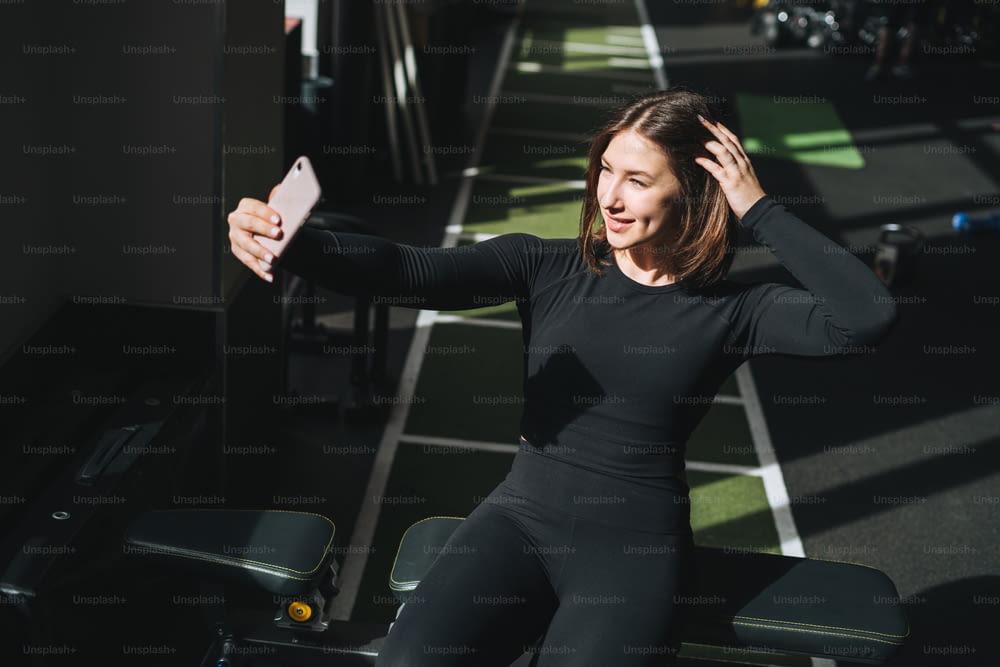 Ritratto di riposo Giovane donna bruna in abbigliamento sportivo attivo che scatta selfie nel fitness club