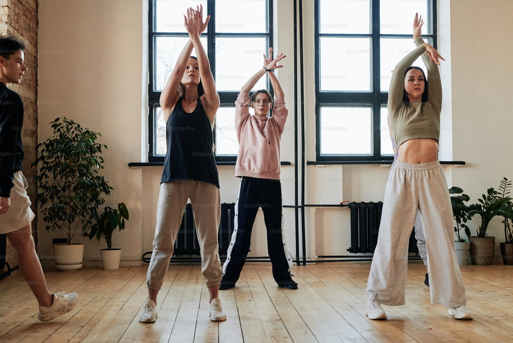 Group of teenage girls and guy raising stretched arms over their heads during exercise of vogue dancing at repetition in loft studio