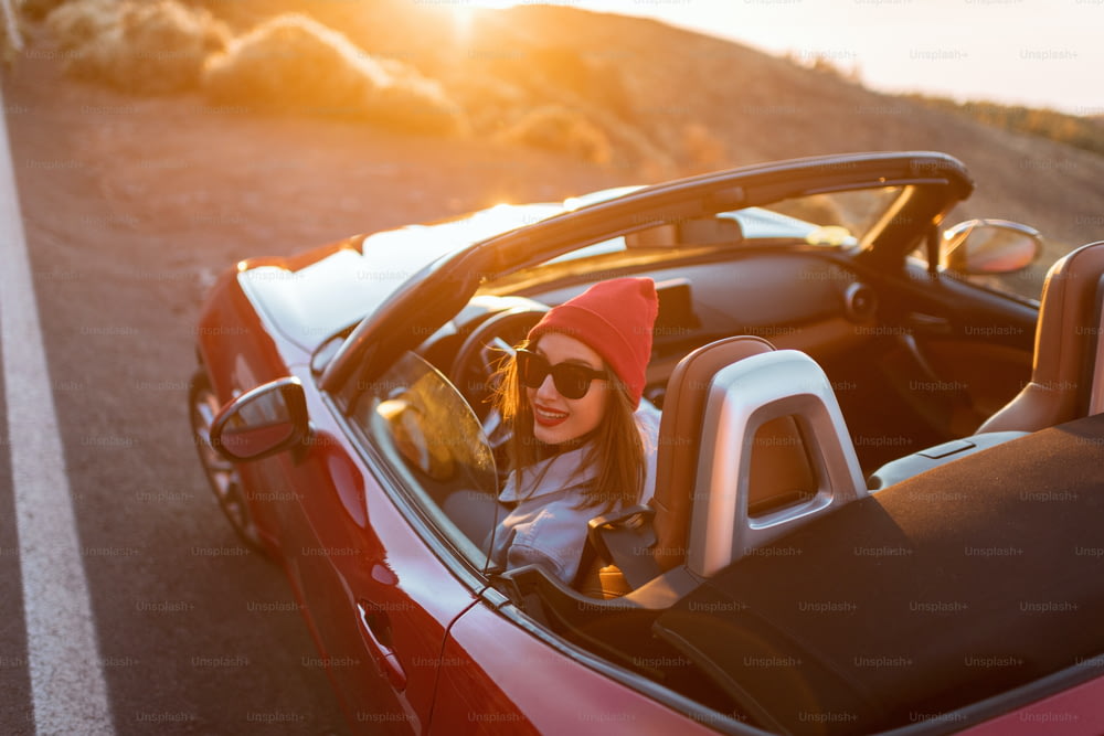 Giovane donna che viaggia in auto su una bella strada di montagna durante un tramonto