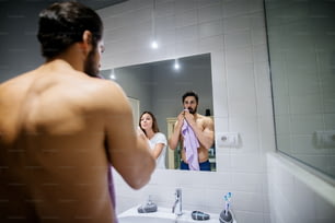 Beautiful handsome nice couple standing together in front of mirror and cleaning their skin in the morning at bathroom.