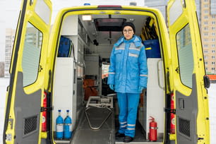 Junge Sanitäterin in Uniform steht an leerer Trage im Krankenwagen vor der Kamera