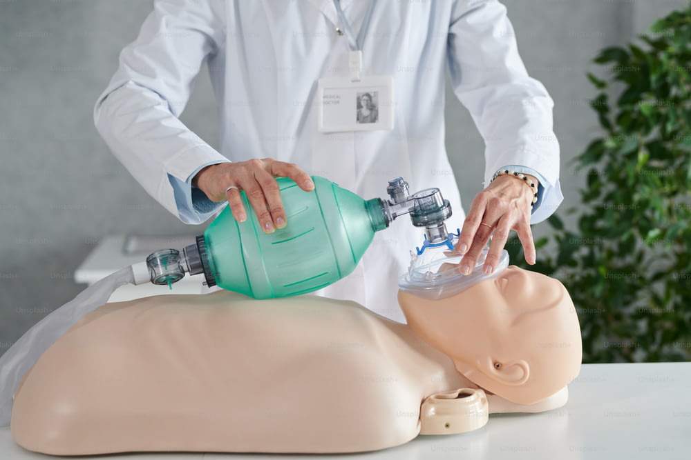 Primer plano de un trabajador médico con bata blanca que demuestra la reanimación del paciente en un maniquí con una máscara de oxígeno