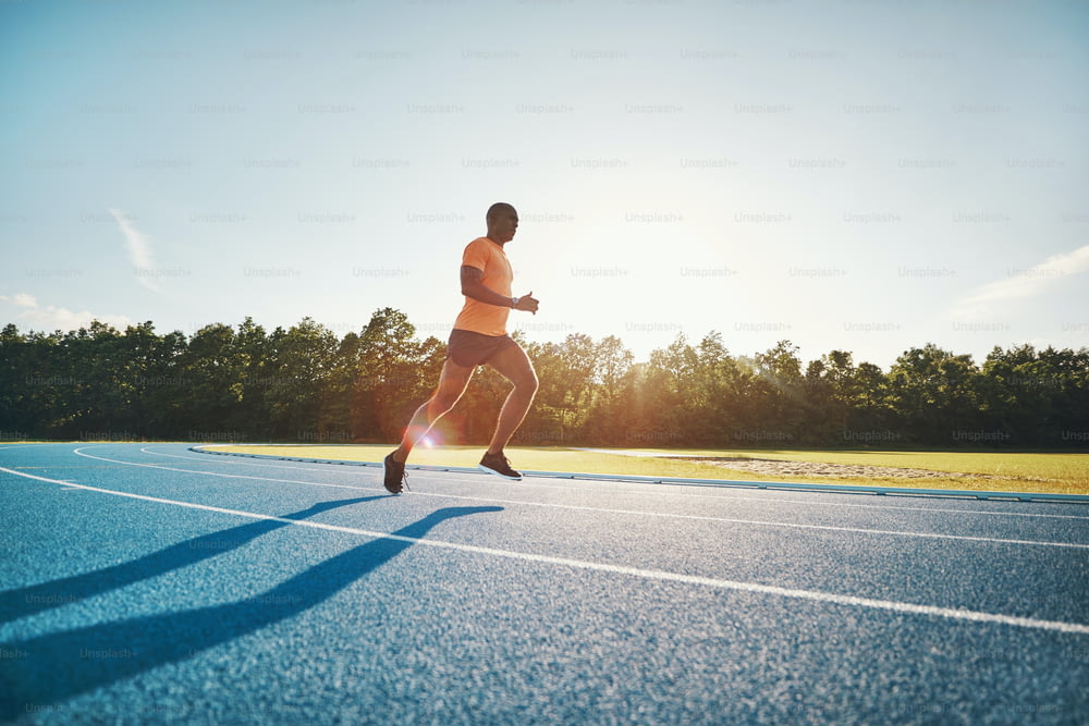 화창한 날 경마장을 따라 달리는 운동복을 입은 집중된 젊은 아프리카 남성 운동 선수