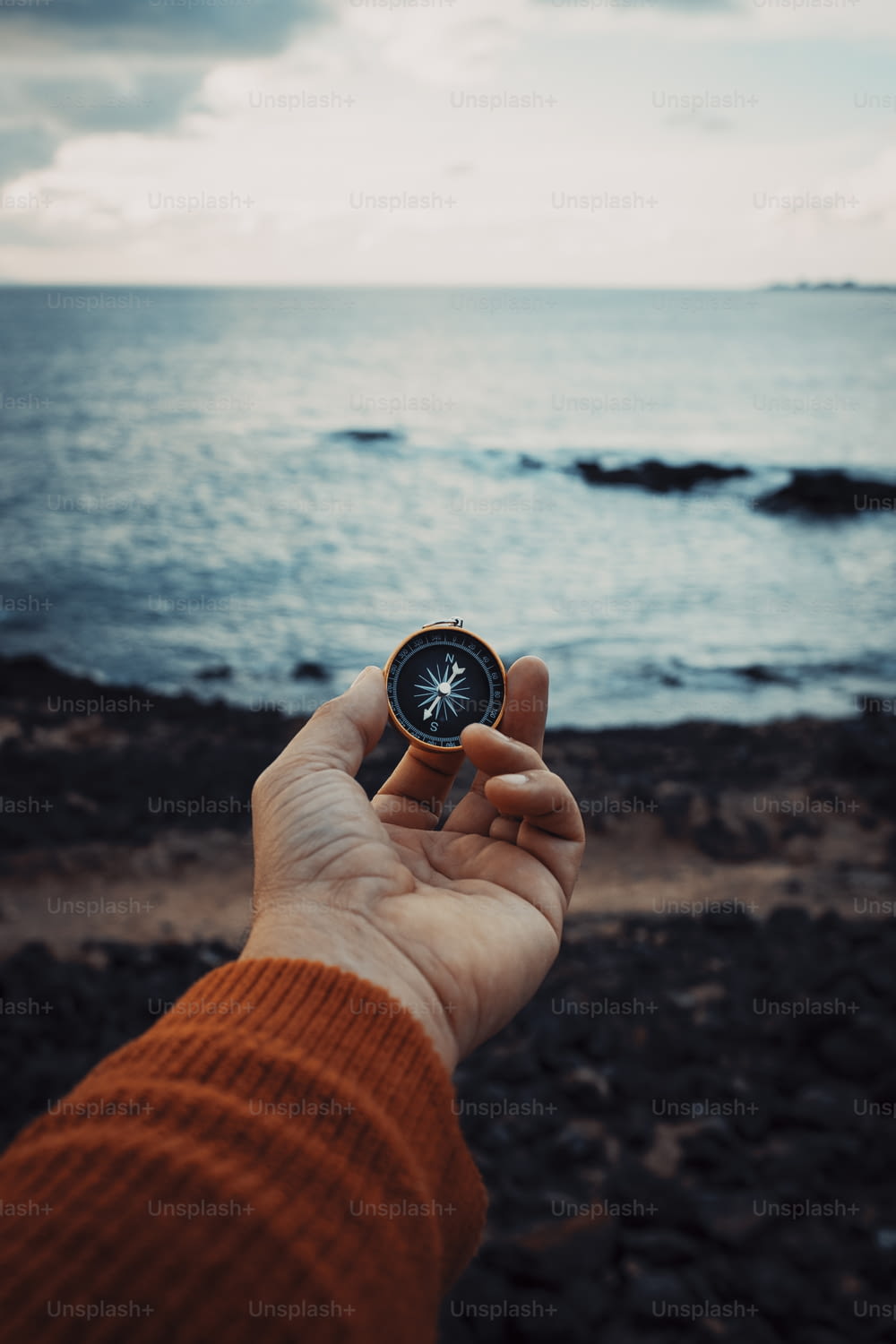 Pov of man hand holding navigational travel compass to find direction and next destination place. Concept of travel people and exploring. Beach and ocean with sky light in background