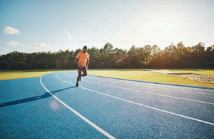 Focused young African male athlete in sportswear sprinting alone along a running track on a sunny day