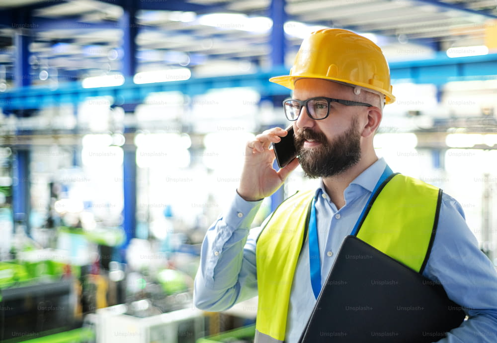Side view of technician or engineer with hard hat standing in industrial factory, using telephone.