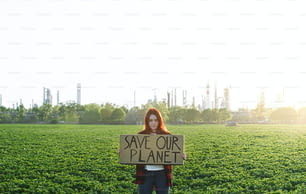 Ritratto di giovane attivista con cartello in piedi all'aperto vicino alla raffineria di petrolio, che protesta.