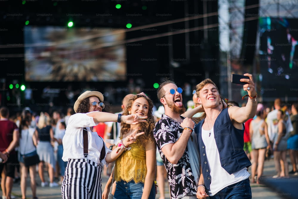 Vista frontal do grupo de jovens amigos com smartphone no festival de verão, tirando selfie.