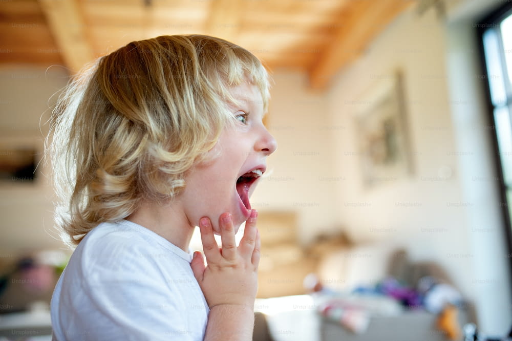 Portrait de vue latérale d’un petit garçon avec la bouche ouverte à l’intérieur à la maison.