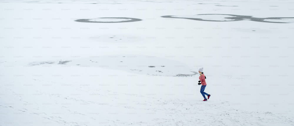 A very long shot of active senior woman running outdoors in snowy winter. Copy space.