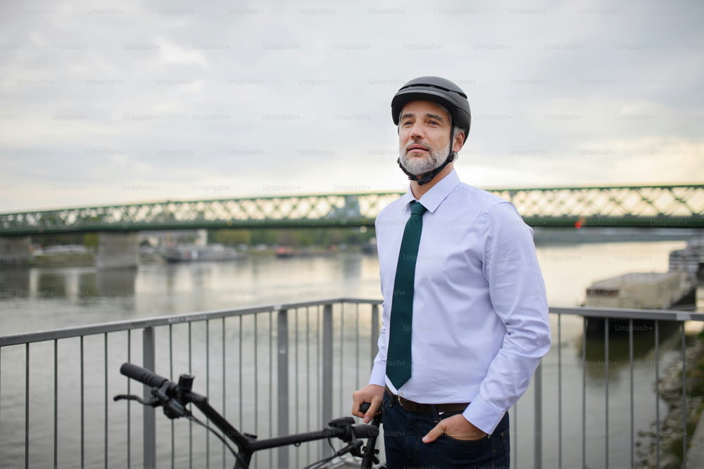 Ein Geschäftsmann pendelt auf dem Weg zur Arbeit, auf Brücke stehend und mit Fahrrad, nachhaltiges Lifestyle-Konzept.