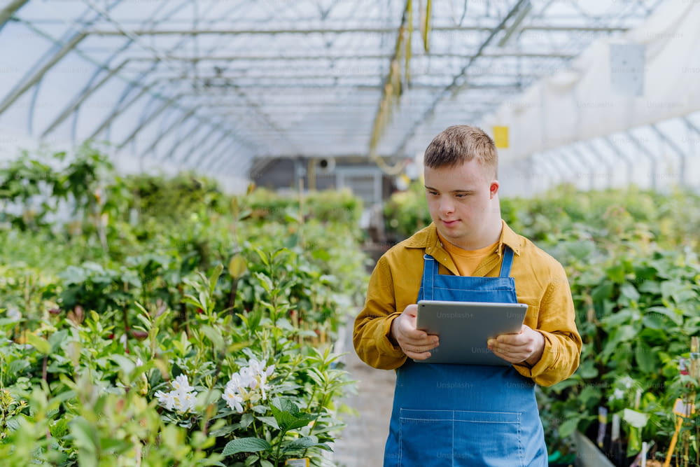 Ein junger Angestellter mit Down-Syndrom, der im Gartencenter arbeitet und auf dem Tablet tippt.