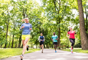 녹색 햇볕이 잘 드는 여름 공원에서 달리는 젊은 운동 선수 그룹.