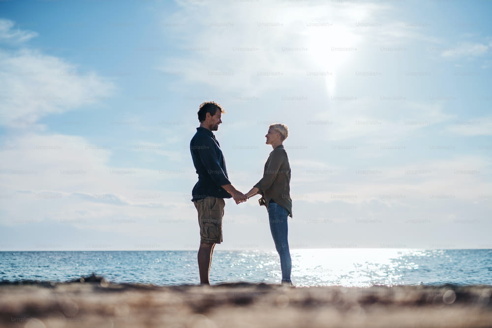 A young couple standing outdoors on beach, holding hands. Copy space.