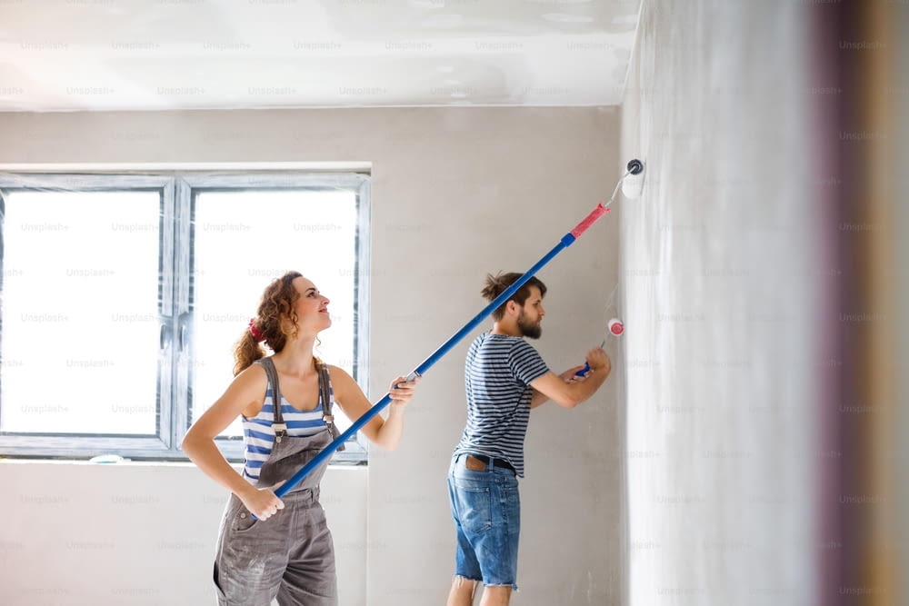 Beau jeune couple s’amusant et peignant les murs à l’aide de rouleaux de peinture dans leur nouvelle maison. Concept de relooking et de rénovation de maison.