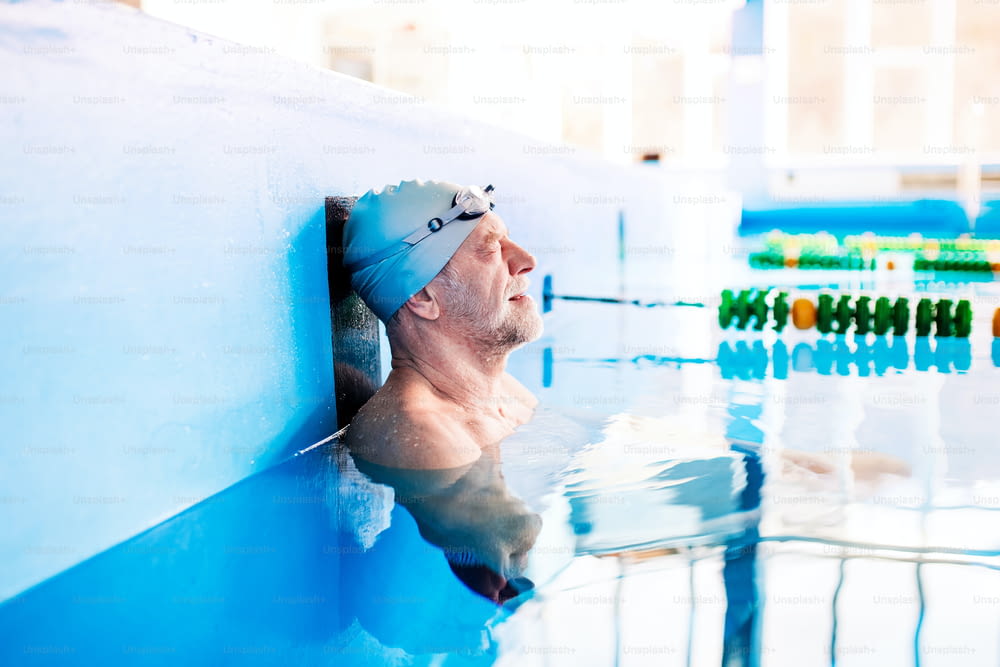 Senior man swimming standing in water in an indoor swimming pool. Active pensioner enjoying sport.