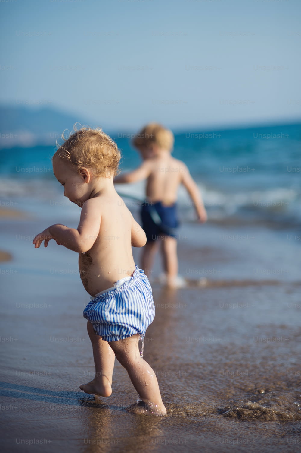 Dos niños pequeños sin camisa caminando por una playa en vacaciones de verano.