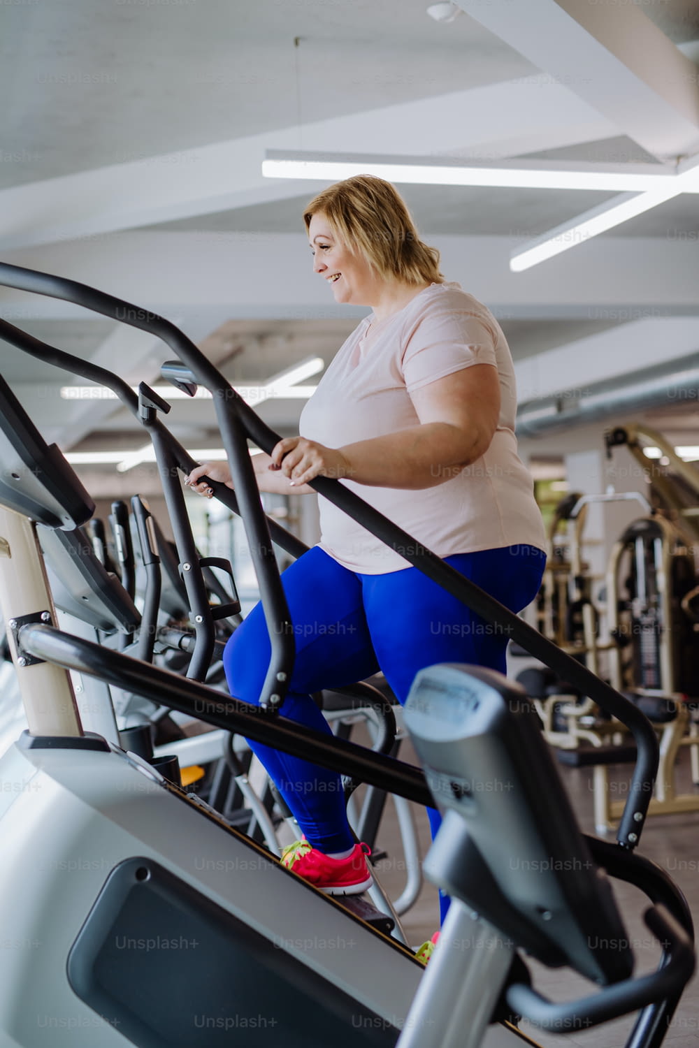 A happy mid adult overweight woman exercising on stepper indoors in gym