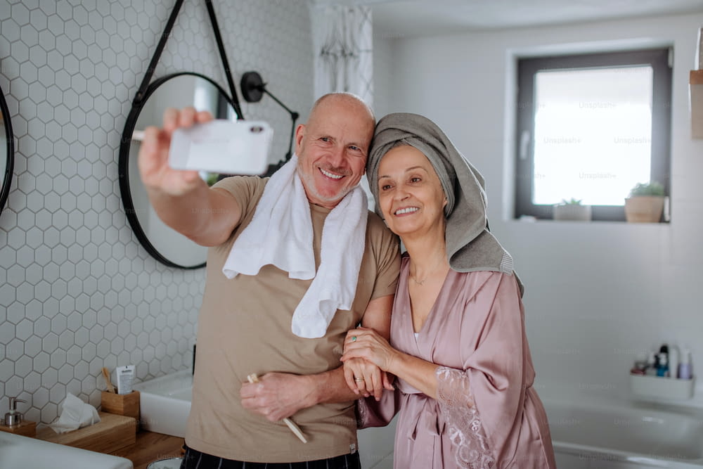 A senior couple in love in bathroom, using smartphone, morning routine concept.