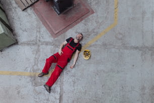 A top view of worker lying on floor after accident in factory. First aid support on workplace concept.