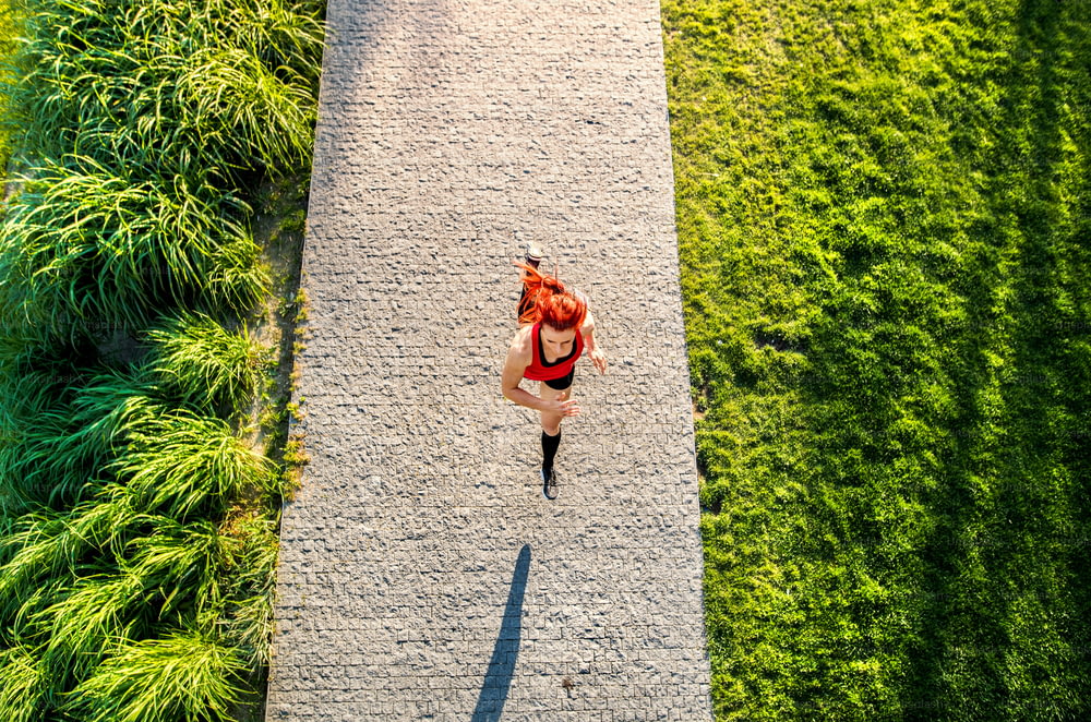 Schöne junge Athletin in Sportkleidung läuft auf Betonweg im grünen sonnigen Park.