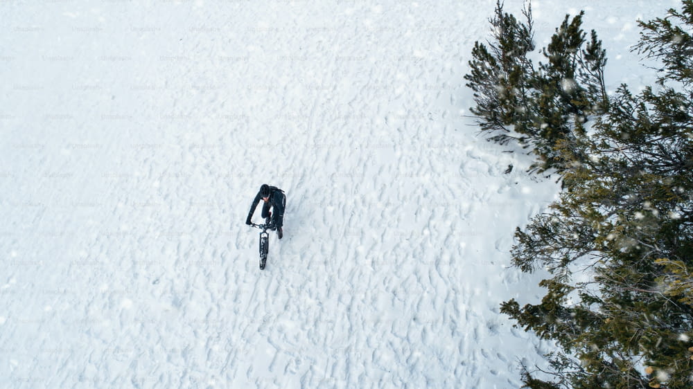 Aerial view of mountain biker riding on snow in forest outdoors in winter. Copy space.