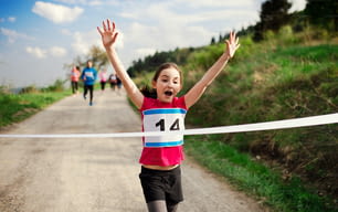 Eine kleine Läuferin überquert die Ziellinie in einem Wettkampf in der Natur.