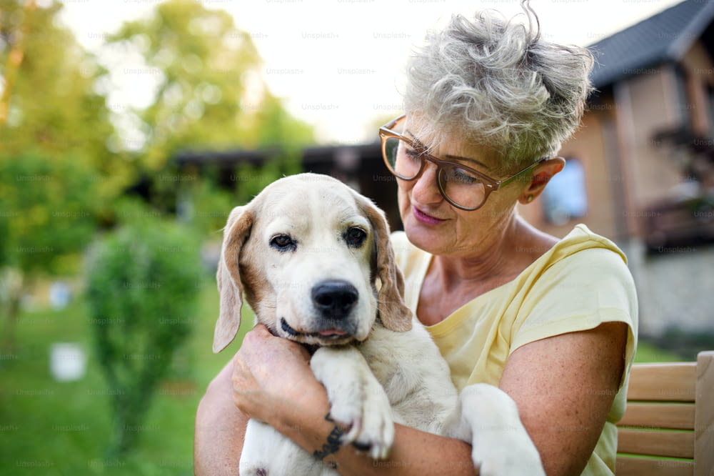 Portrait of senior woman standing and resting outdoors in garden, holding pet dog.