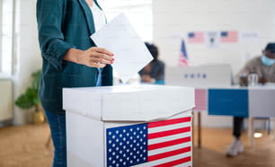 Nicht erkennbare Frau, die ihre Stimme in die Wahlurne gibt, USA-Wahlen und Coronavirus-Konzept.