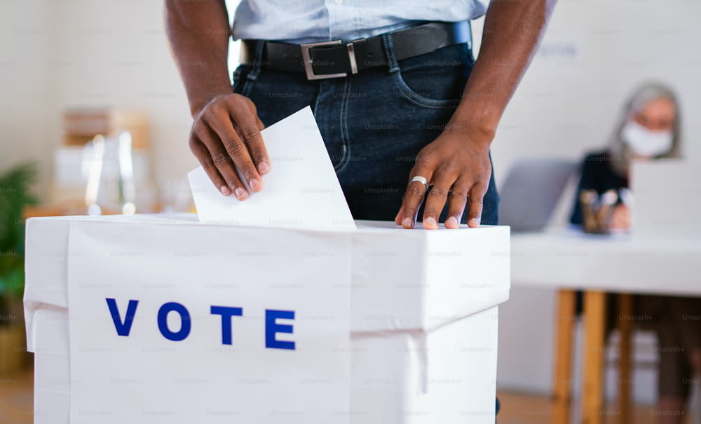 Homem afro-americano irreconhecível colocando seu voto nas urnas, eleições nos EUA e conceito de coronavírus.