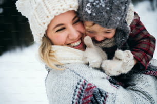Retrato da mãe alegre com a filha pequena em pé na natureza do inverno, rindo.