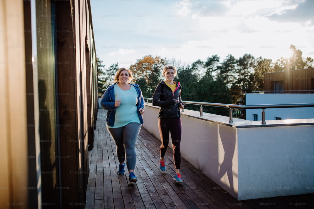 An overweight woman running and exercising with personal trainer outdoors on gym terrace.