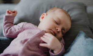 a Portrait of newborn baby girl, sleeping an lying on sofa indoors at home.