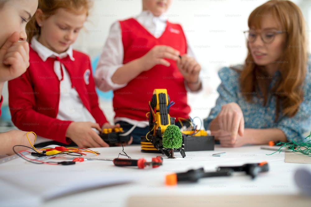 A group of kids with young science teacher programming electric toys and robots at robotics classroom