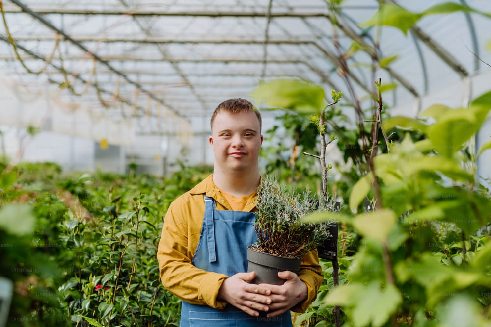 Ein glücklicher junger Mitarbeiter mit Down-Syndrom, der im Gartencenter arbeitet und sich um Blumen kümmert.