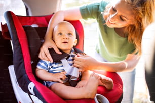 Jeune mère mettant son petit garçon dans le siège auto, attachant les ceintures de sécurité.