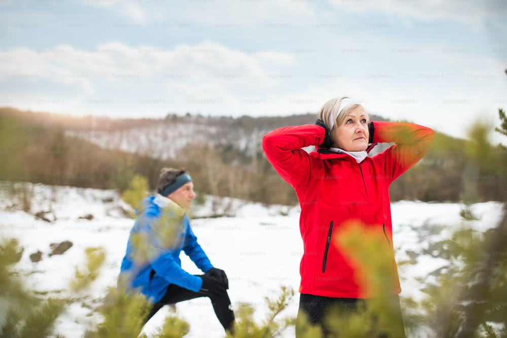 Senior couple jogging outside in winter nature, stretching.