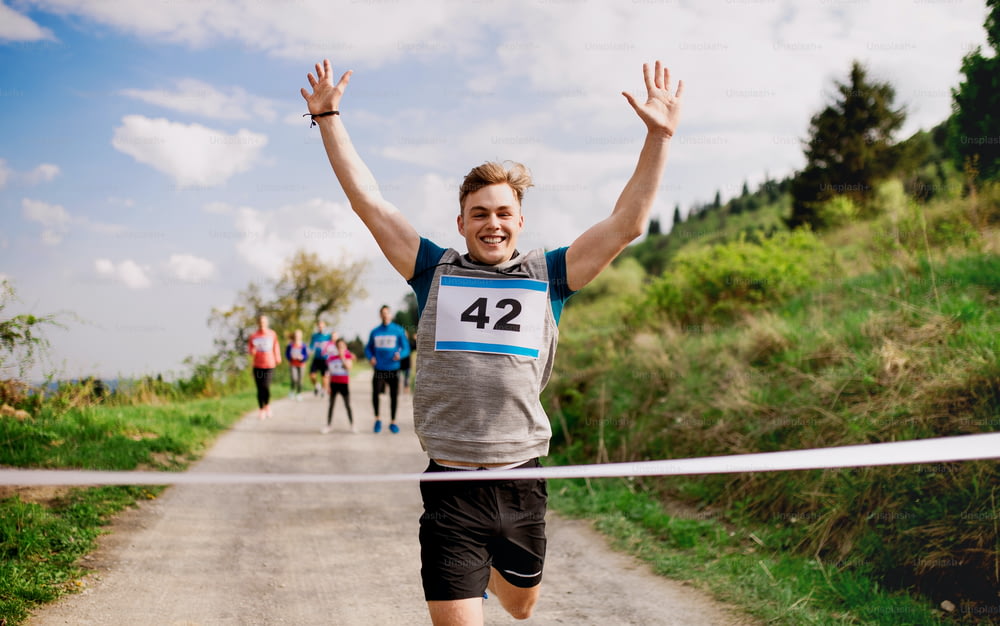 A young man runner crossing finish line in a race competition in nature, arms raised.