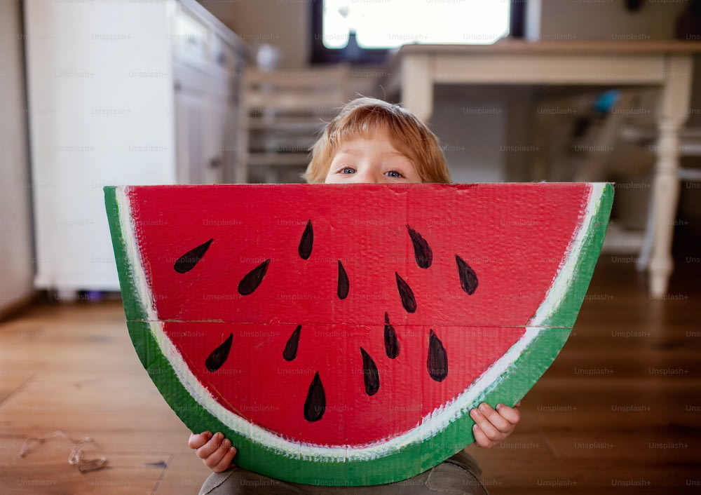 Un niño pequeño jugando con una gran fruta de juguete en el interior de la casa, comiendo el concepto de fruta.