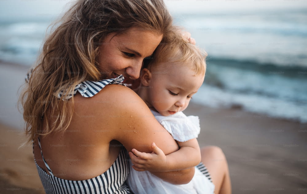 Un primer plano de una madre joven con una niña pequeña en la playa en vacaciones de verano.