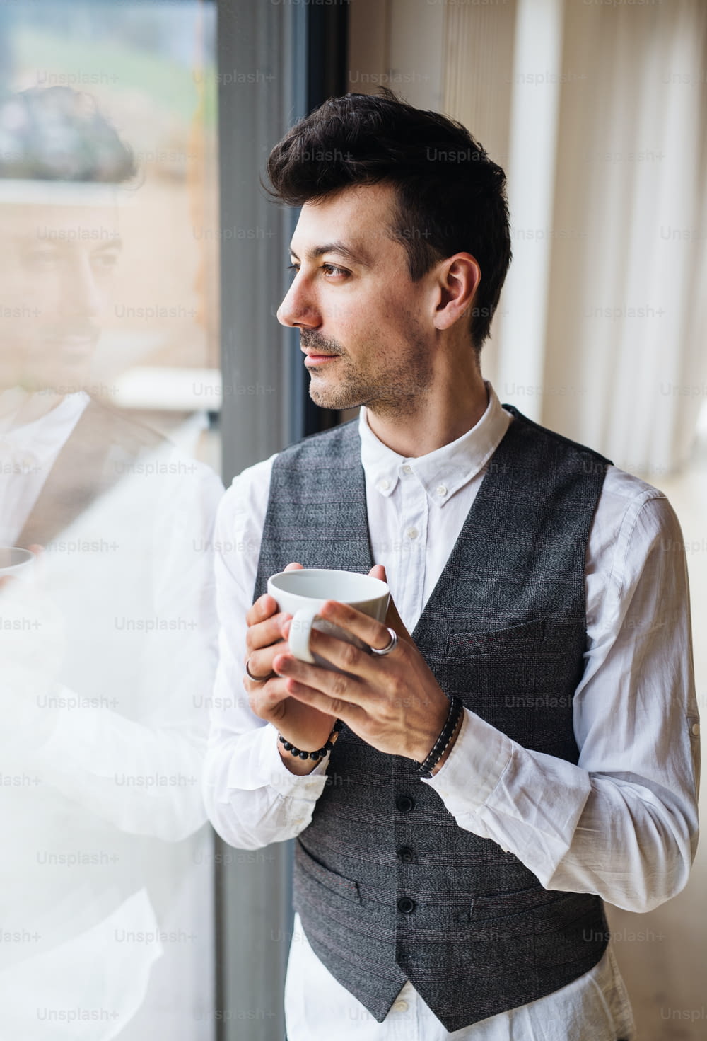 A young man with coffee standing by the window. Copy space.