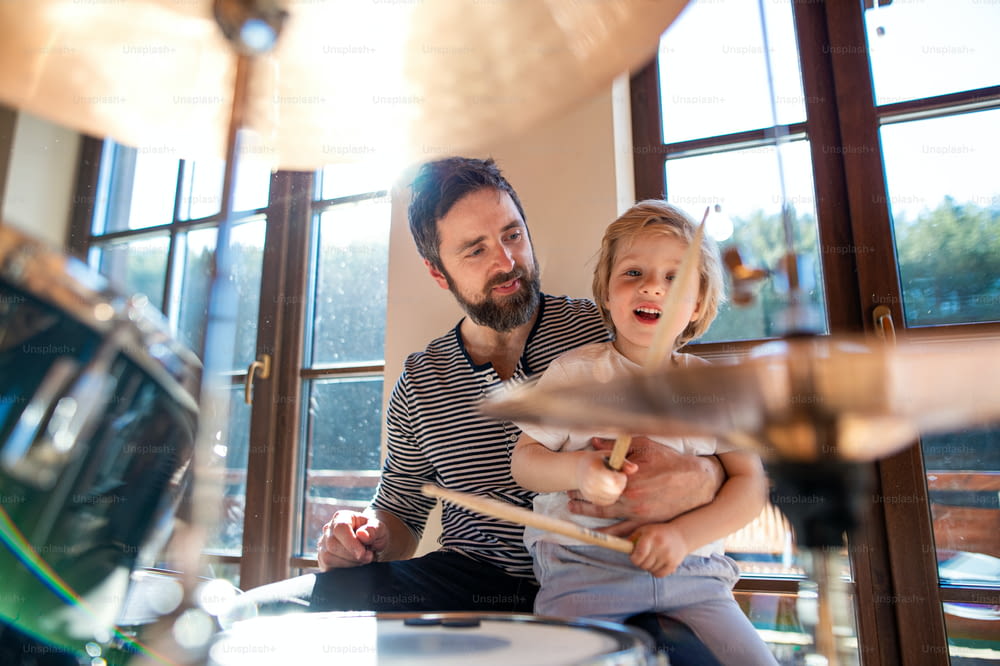Front view of portrait of small boy with father indoors at home, playing drums.