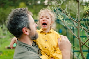 泣き叫ぶ幼い娘を抱きかかえ、庭で慰める父親