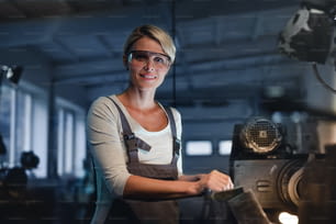 Un ritratto di donna industriale adulta che lavora all'interno in un'officina metallica, guardando la macchina fotografica.