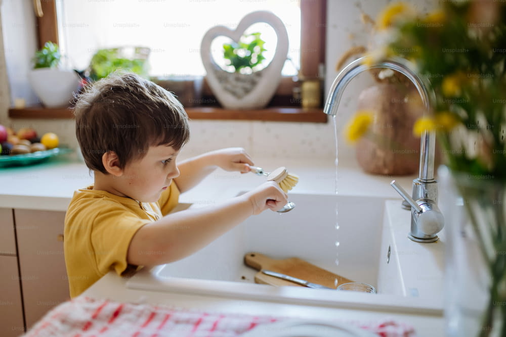 Un ragazzino che lava la tazza nel lavandino in cucina con uno scrub in legno, sostenibile lifestlye.
