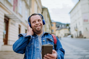 通りを歩いているときに音楽を聴くダウンシドロームの幸せな青年。