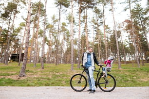Young father with his daughter in bicycle seat in warm clothes cycling together outside in autumn nature.