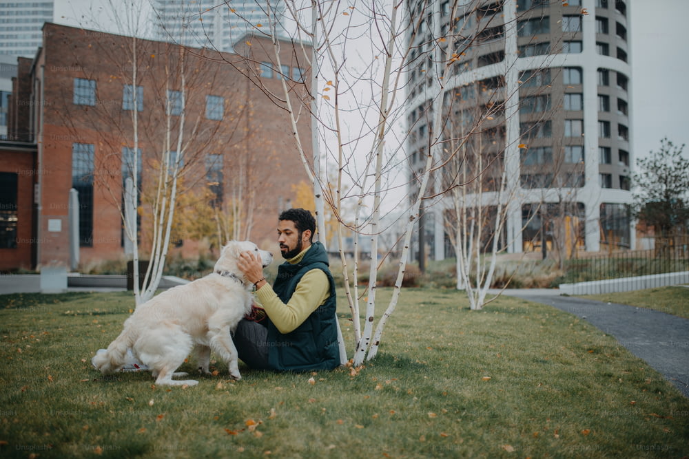 街の屋外で犬と一緒に芝生に座っている幸せな青年。