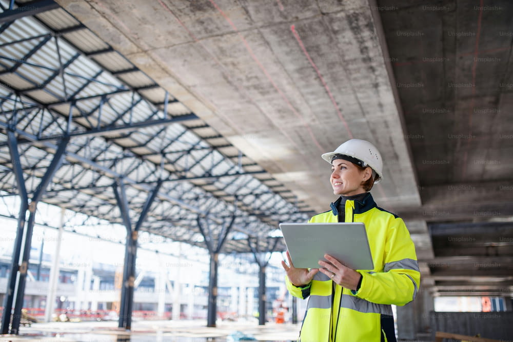 A woman engineer with tablet standing on construction site, working. Copy space.